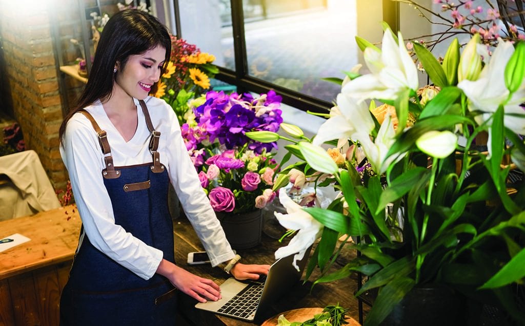 young smiling female on a laptop at a flower shop Use LinkedIn to reach corporate clients, demonstrate your community connections and source helpful business tips.